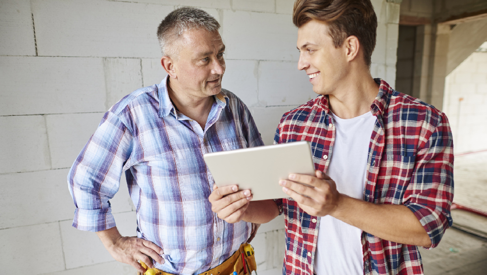 Contractor and apprentice reviewing project details on tablet at construction site