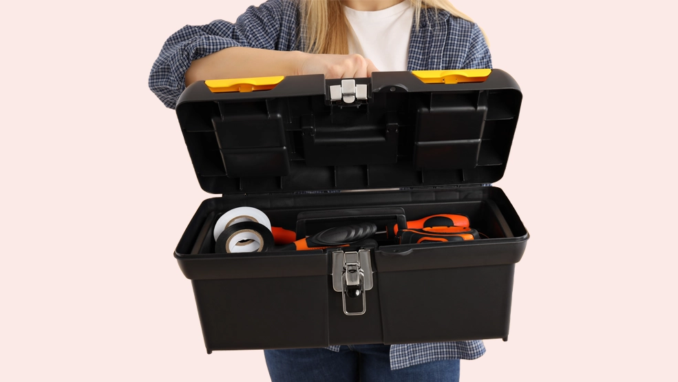 Woman holding open black toolbox containing tape, screwdrivers, and hand tools
