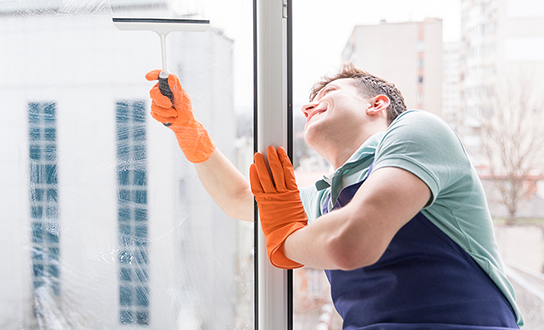 Window cleaner in orange gloves using a squeegee on exterior glass in a residential high-rise building