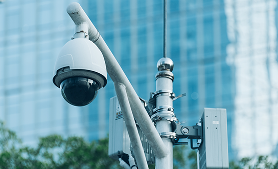Dome security camera mounted on pole with modern glass office building in background