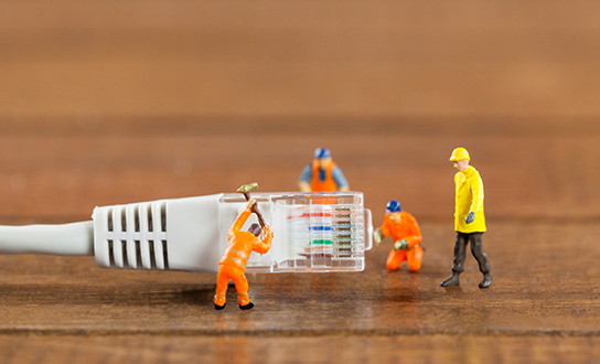Miniature construction workers assembling an ethernet cable connector on a wooden surface