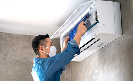 HVAC technician wearing a mask while servicing a wall-mounted air conditioning unit
