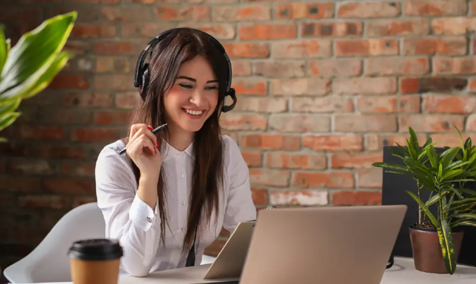 Customer service representative with headset smiling while working on laptop in modern office