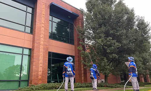 Exterior cleaning crew using water-fed poles to wash windows on a two-story commercial brick building