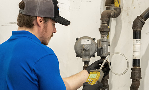 HVAC technician using a gas leak detector to inspect piping system