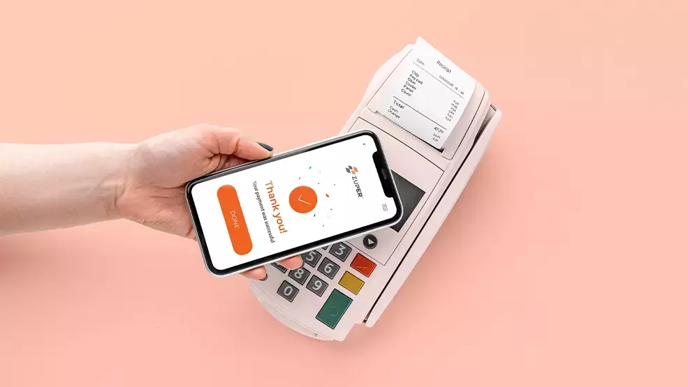 Smartphone displaying Zuper payment confirmation screen held over a point-of-sale terminal printing a receipt