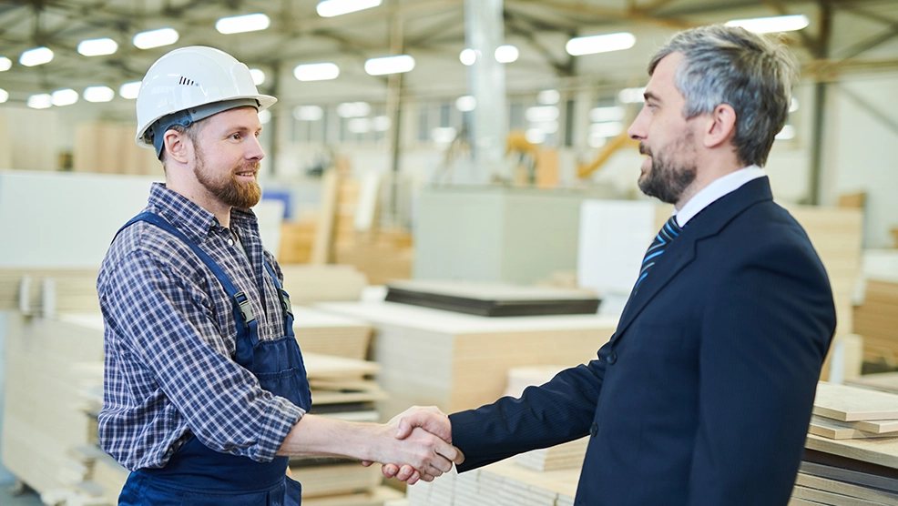 Contractor in hard hat shaking hands with business professional in a warehouse facility