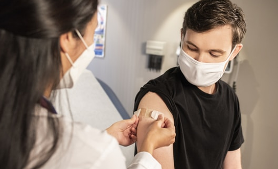 Healthcare worker applying bandage to patient's upper arm after vaccination in clinical setting