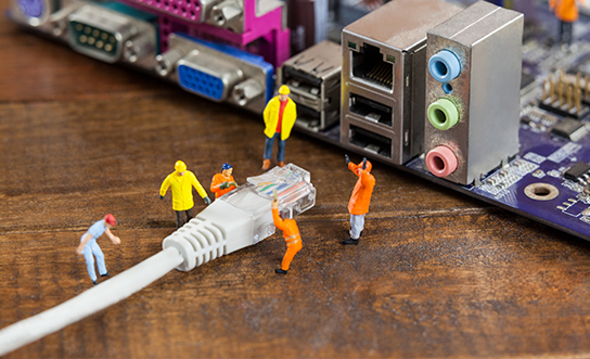 Miniature worker figurines positioning an Ethernet cable near computer motherboard ports