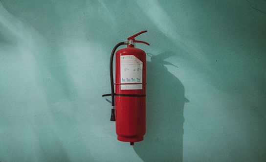Red fire extinguisher mounted on a teal wall