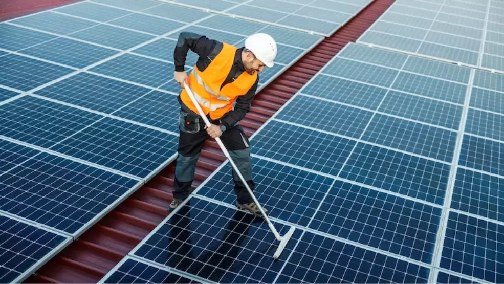 Solar panel technician in safety gear cleaning rooftop panels with a squeegee mop