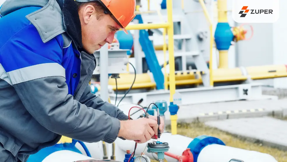 Technician in safety gear using multimeter to test pressure gauge on industrial pipeline