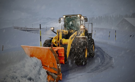 Snow plow loader clearing a snowy road during a winter storm