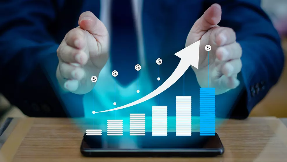Businessman with hands framing a holographic bar chart showing upward financial growth with dollar signs on a tablet