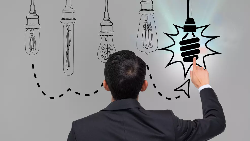 Businessman pointing to illuminated CFL bulb representing innovative idea selection among traditional lightbulb options