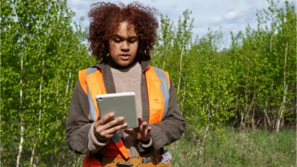 Field technician in safety vest uses tablet to collect data at outdoor job site