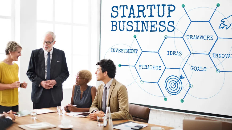 Diverse startup team discussing business strategy with whiteboard showing investment, ideas, teamwork, and goals diagram