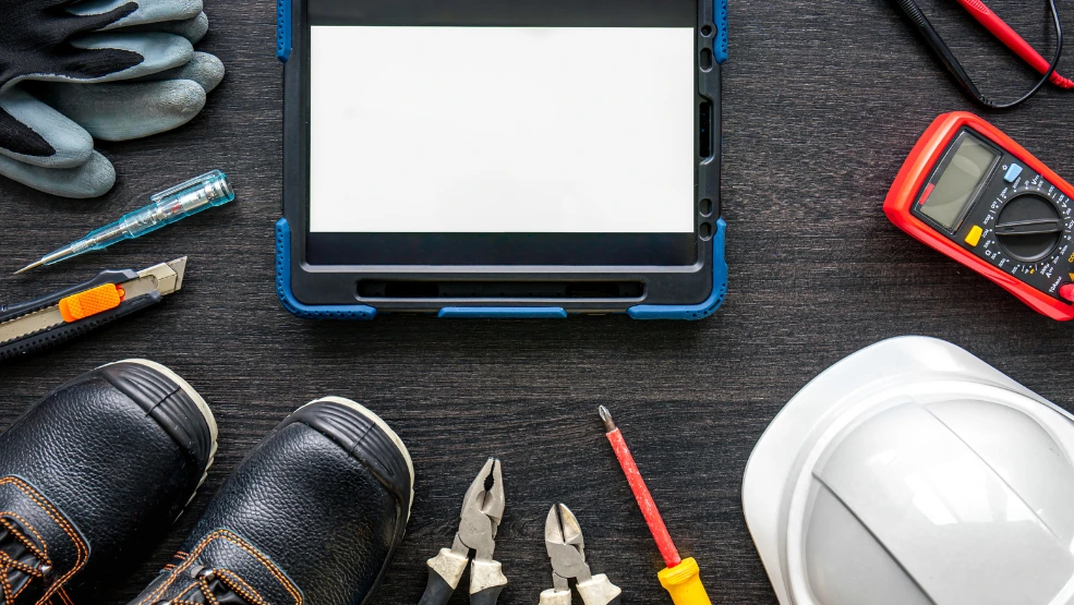 Electrician tools and tablet with blank screen on dark wooden surface with hard hat and multimeter
