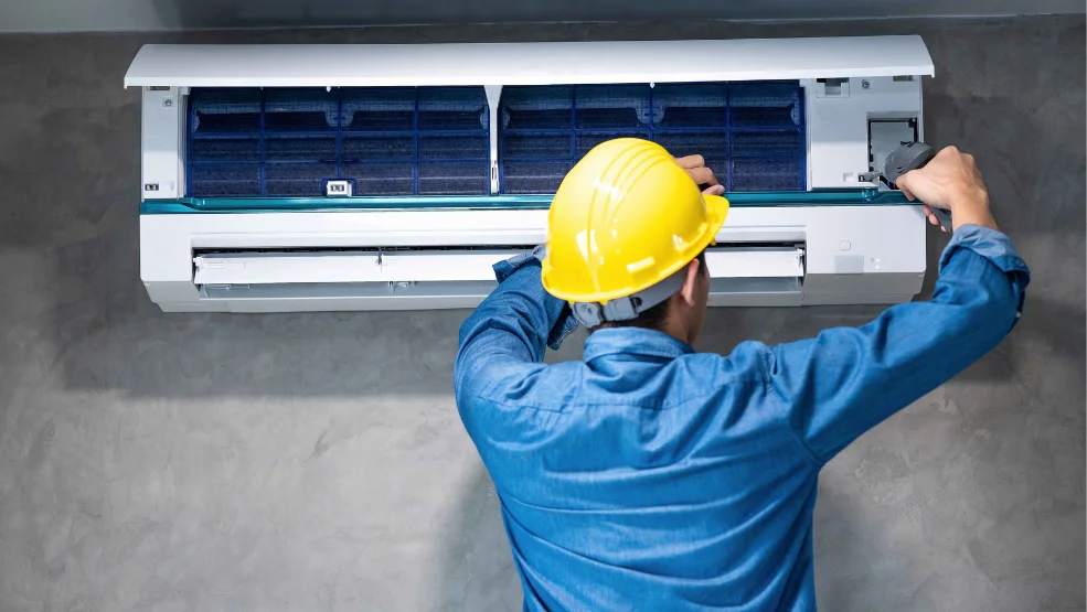 HVAC technician in hard hat servicing a wall-mounted mini-split air conditioning unit