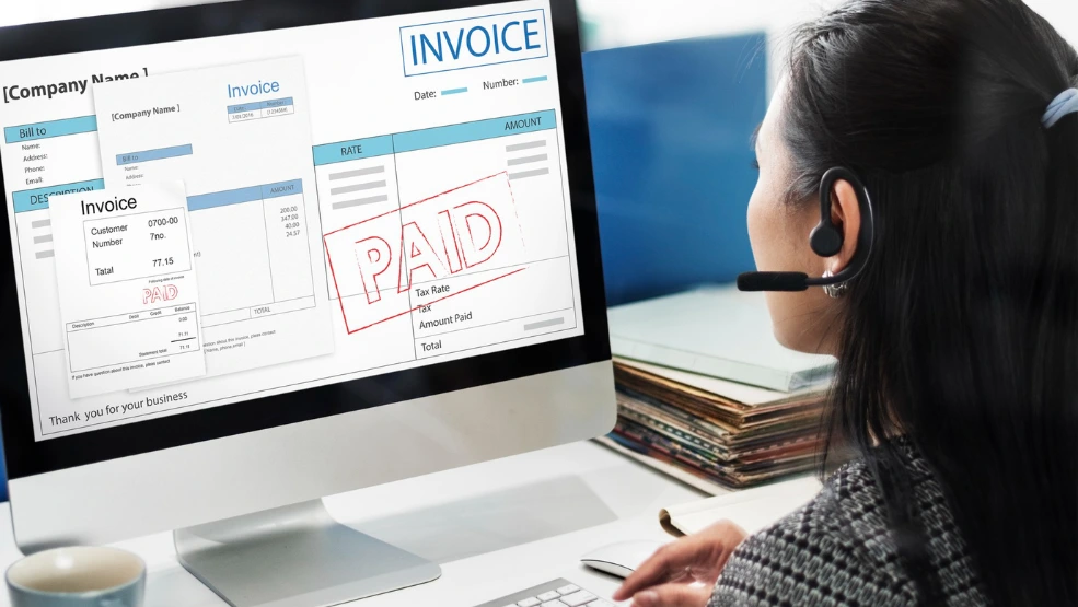 Field service professional reviewing paid invoices on computer screen with billing and payment details displayed