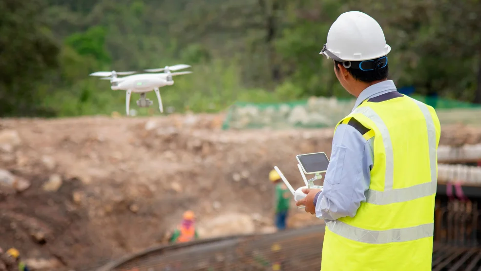 Construction worker in hard hat and safety vest operating a drone with remote controller at job site