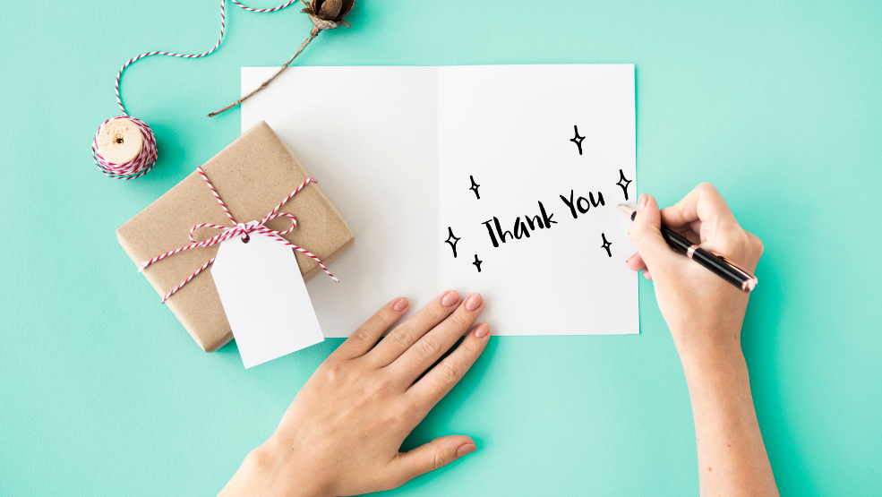Thank you card with decorative sparkles on a teal background next to a kraft paper gift box with twine