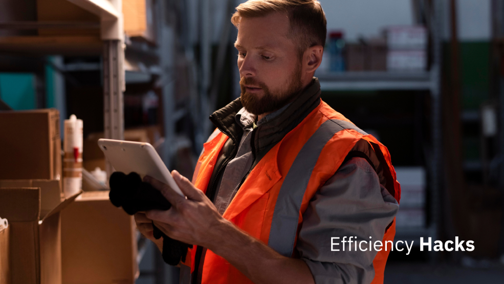 Warehouse worker in safety vest using tablet to check inventory on shelving unit