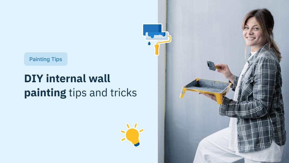 Woman holding paint tray and brush smiling while painting an interior wall gray