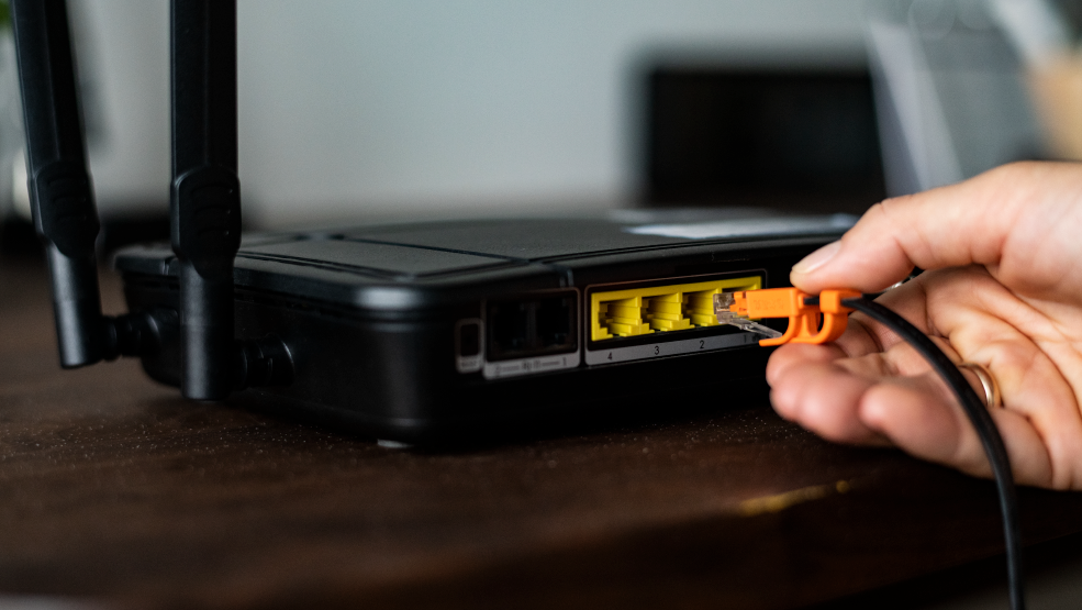 Technician plugging an orange Ethernet cable into a wireless router's LAN port