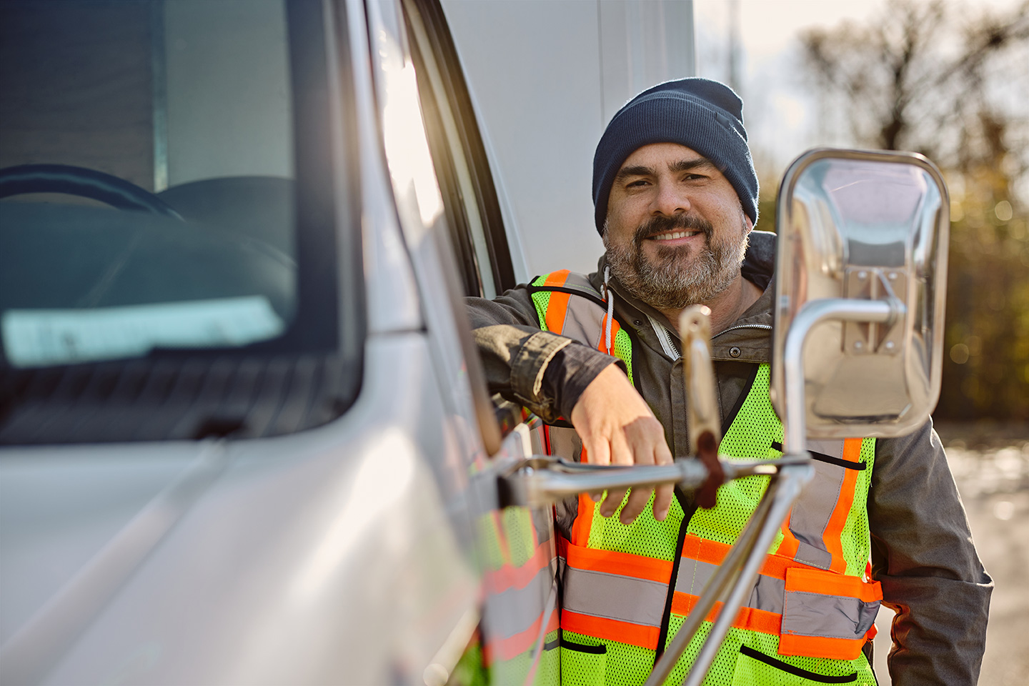 Smiling truck driver in high-visibility vest standing beside commercial vehicle cab