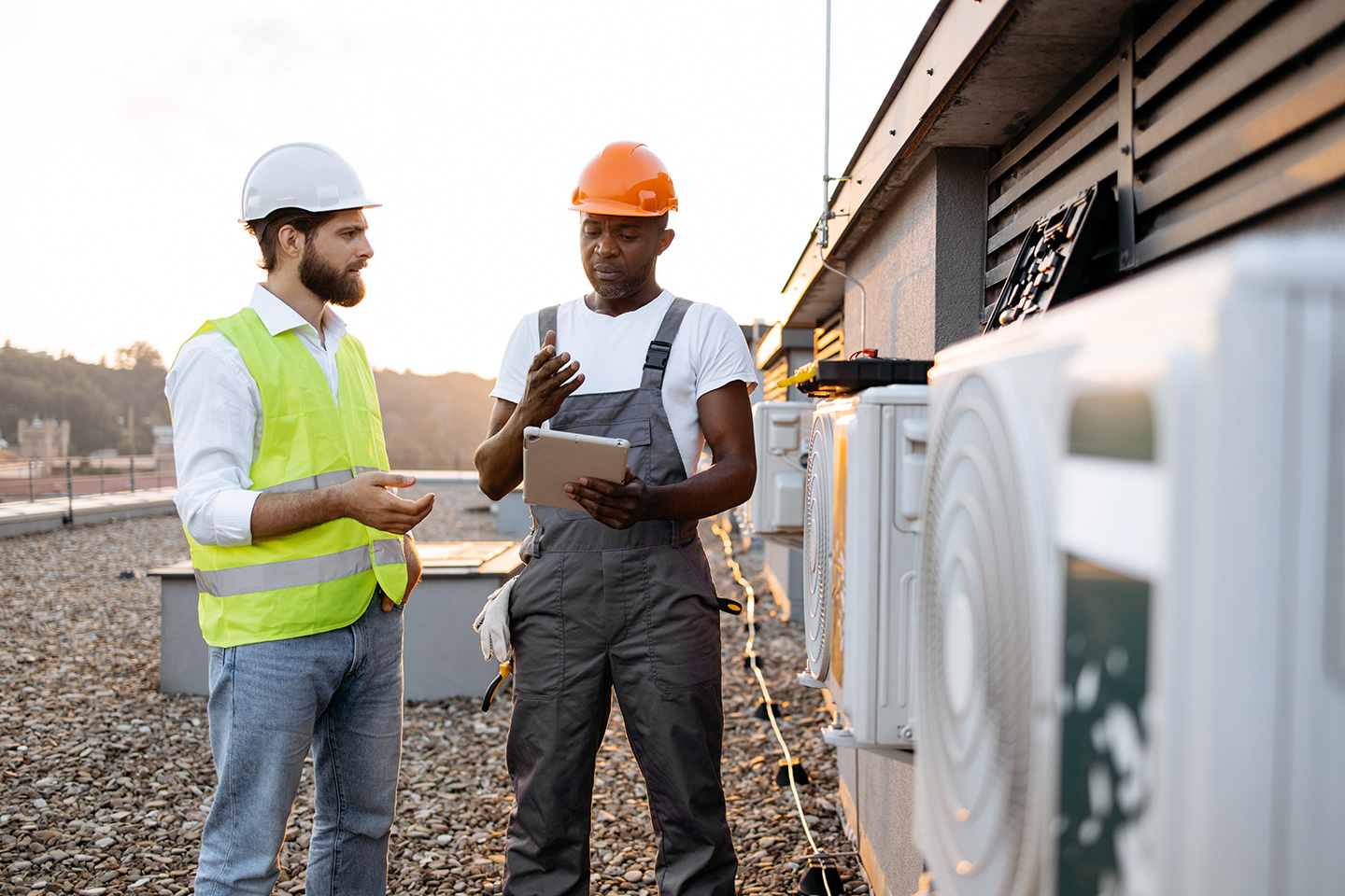 Two technicians reviewing HVAC equipment data on a tablet during a commercial rooftop unit inspection