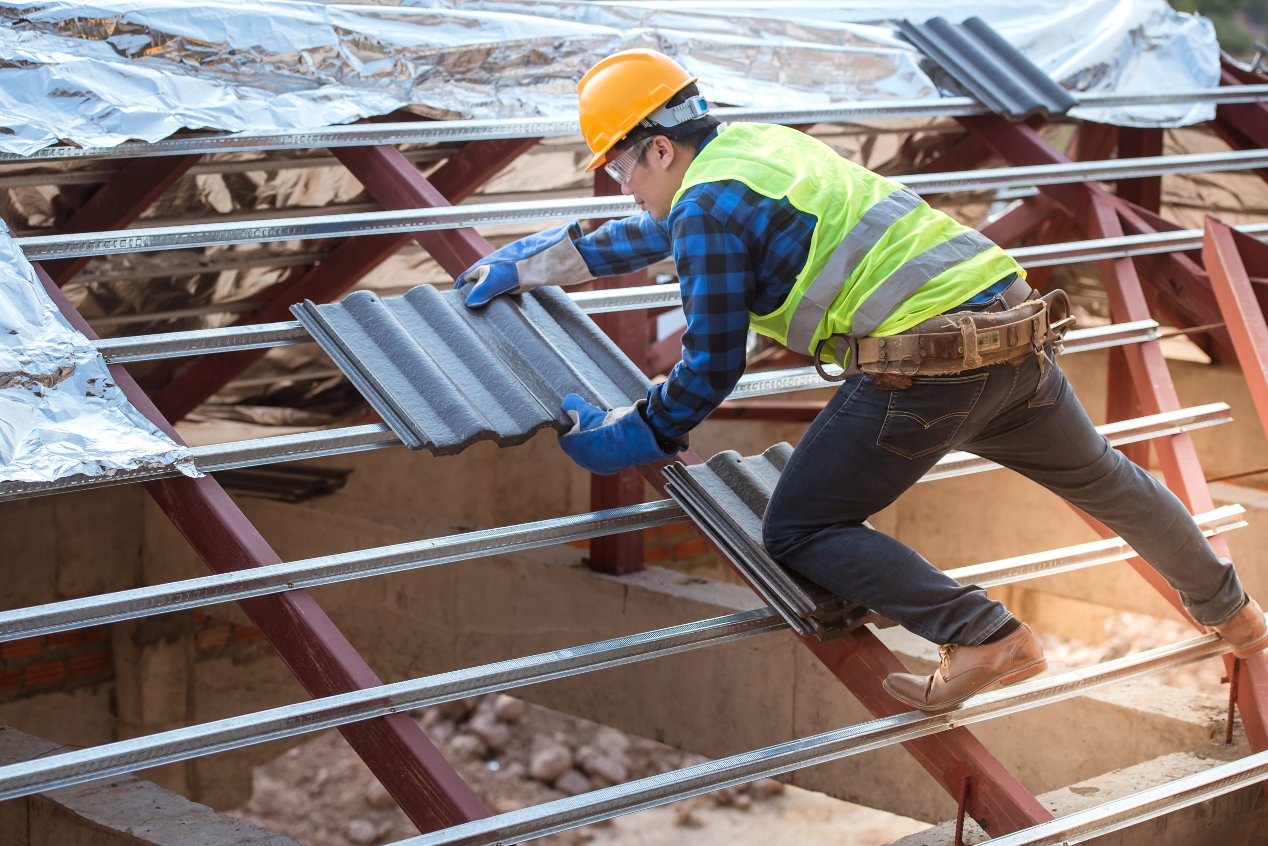 Roofer installing corrugated metal roofing tiles on steel frame structure at construction site