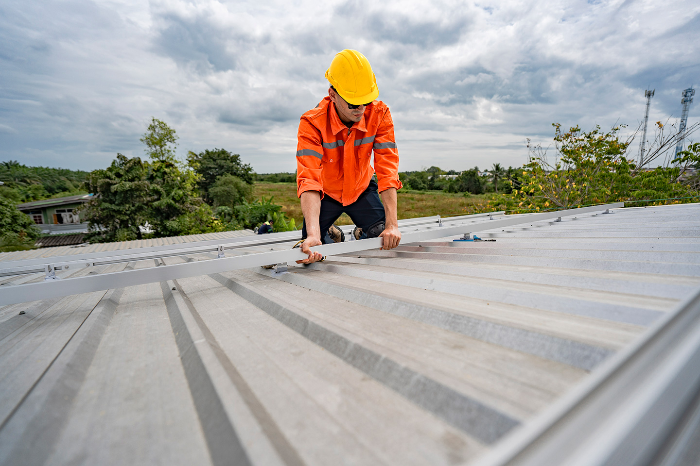 Roofing technician in safety gear installing metal rail mounts for solar panel system on commercial roof