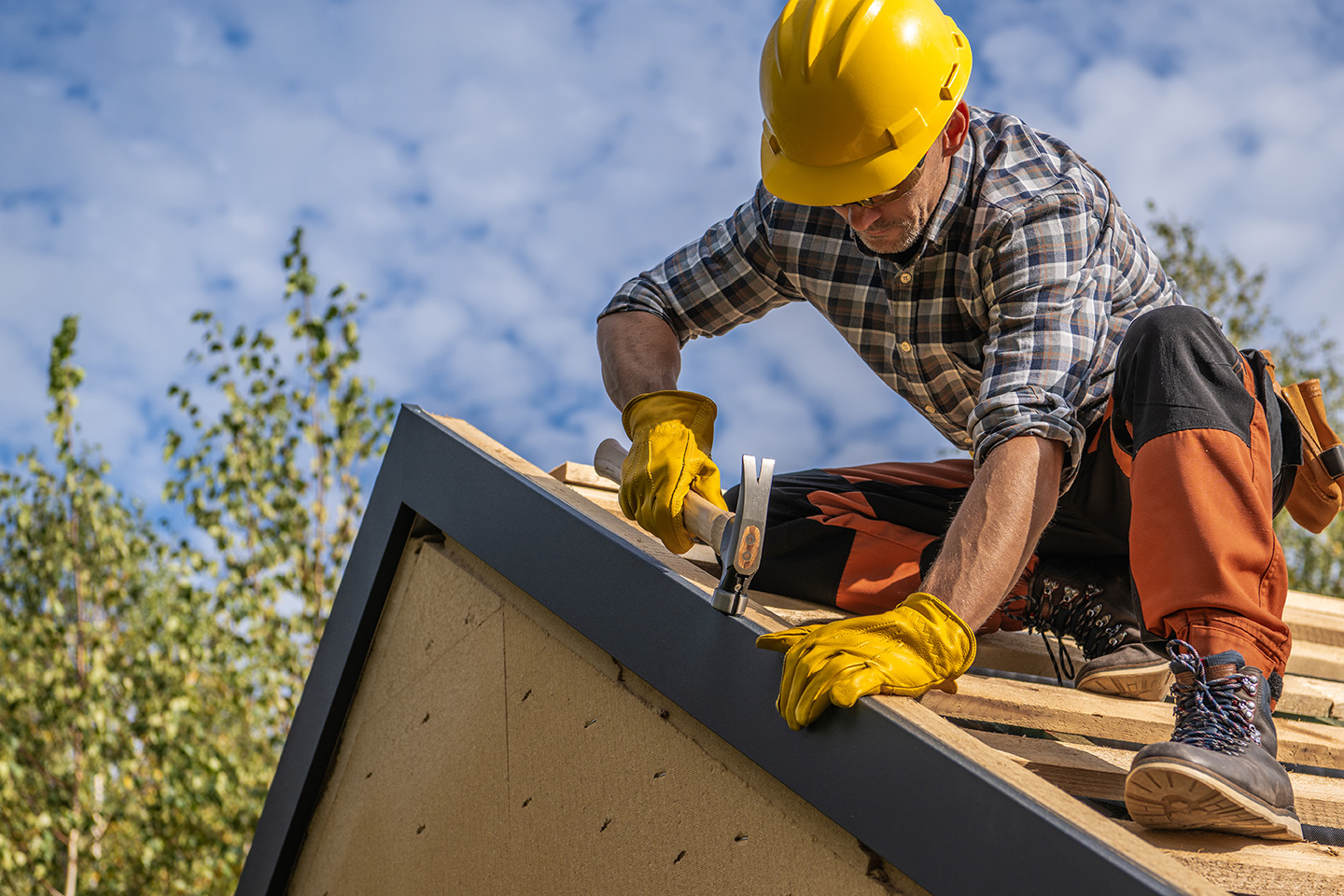 Roofer in hard hat hammering nails into roof ridge cap on a sunny day