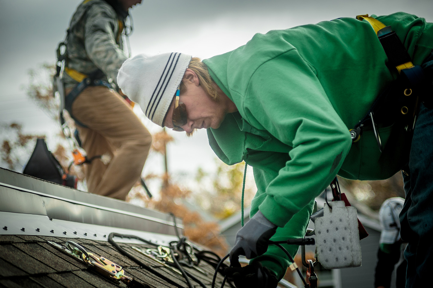 Roofing technician in safety harness installing solar panel mounting rails on residential shingle roof